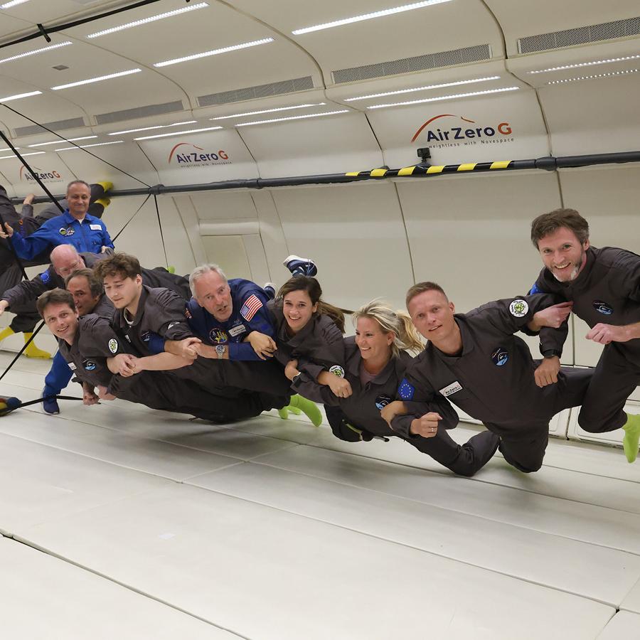 Gruppe von Menschen in Overalls schwebt in einem Flugzeug, das Schwerelosigkeit simuliert.