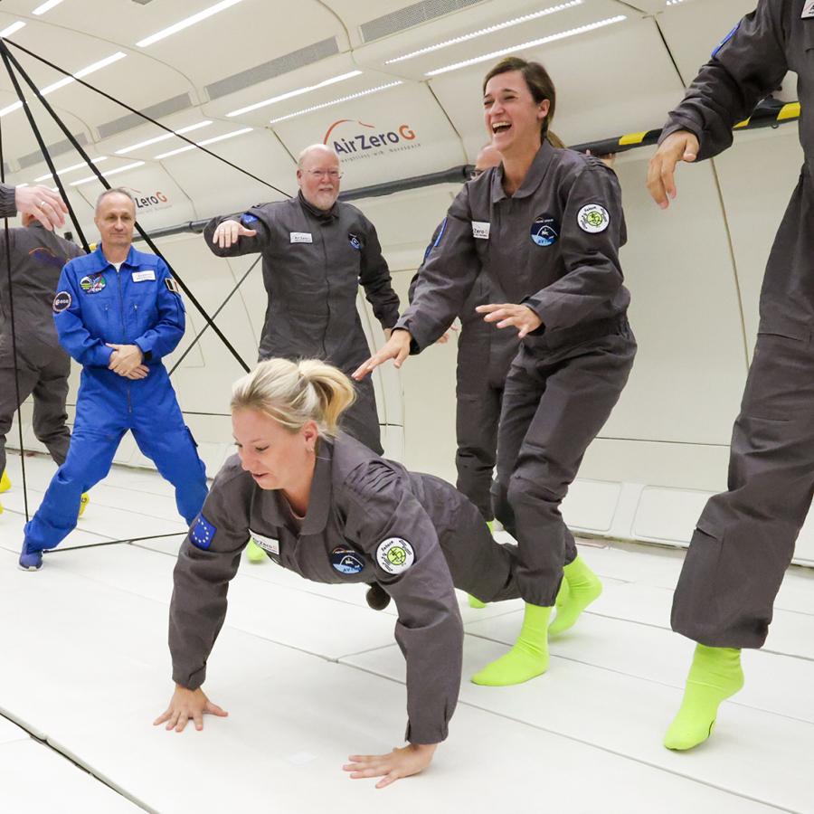 Melanie und Daniela in Overalls und leuchtend grünen Socken machen Übungen in einem Schwerelosigkeitsflugzeug.