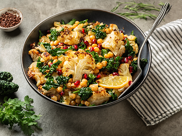 Gerösteter Blumenkohl-Kichererbsen-Salat mit Grünkohl, Granatapfelkernen und Zitrone in einer Schüssel.