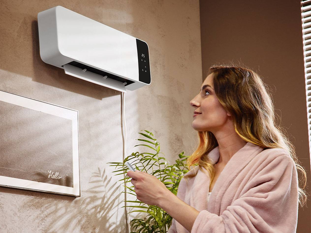 Frau im Bademantel stellt wandmontierte Klimaanlage mit Fernbedienung ein.