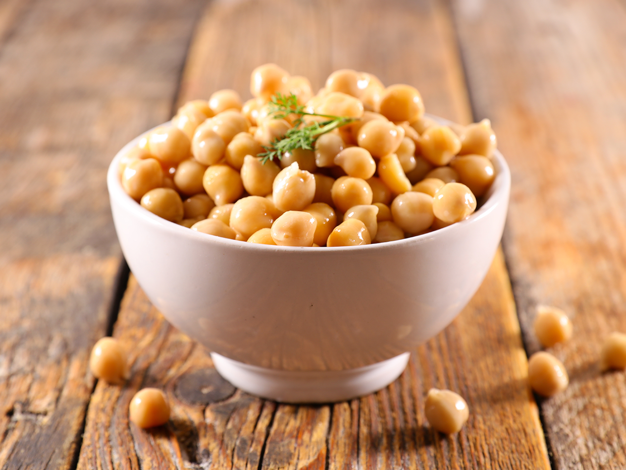 Eine Schale mit Kichererbsen, garniert mit einem kleinen Zweig Dill, auf einem Holztisch.