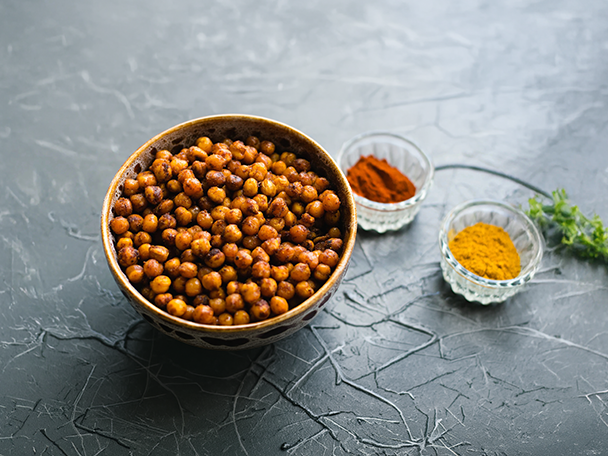 Geröstete Kichererbsen in einer Schale mit Paprika- und Currypulver daneben.