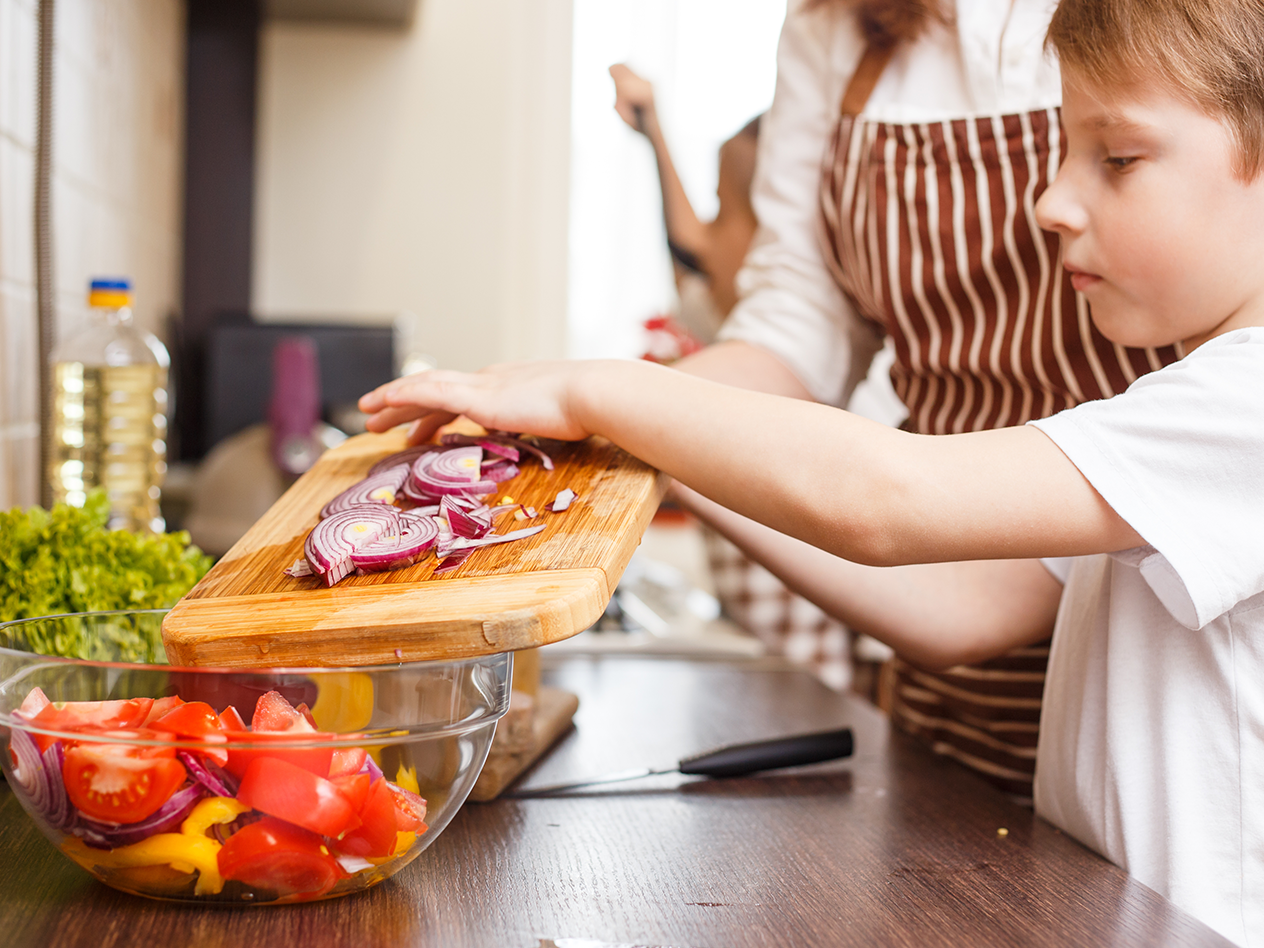 Kind und Erwachsener bereiten gemeinsam einen Salat mit Zwiebeln, Tomaten und Paprika zu.