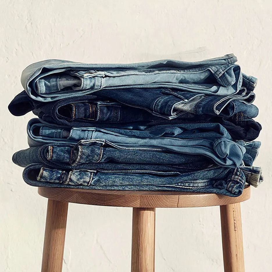 Ein Stapel Jeans in verschiedenen Blautönen auf einem Holzhocker.