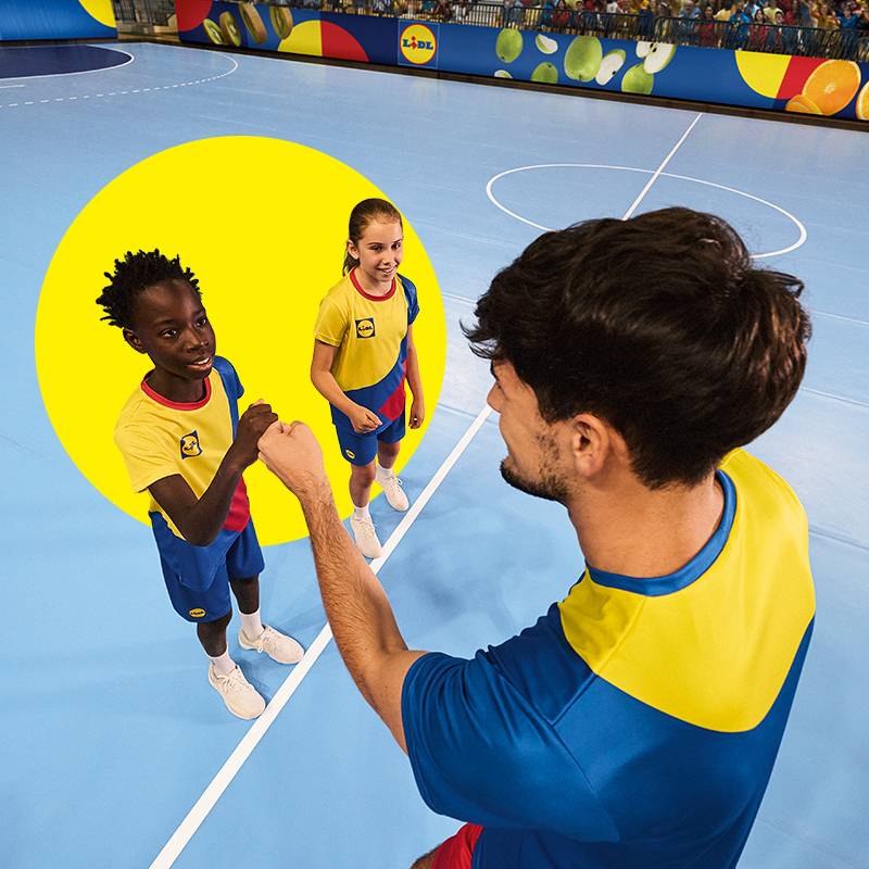 Kinder in Lidl-Sportkleidung geben einem Erwachsenen auf einem Indoor-Spielfeld High-Five.
