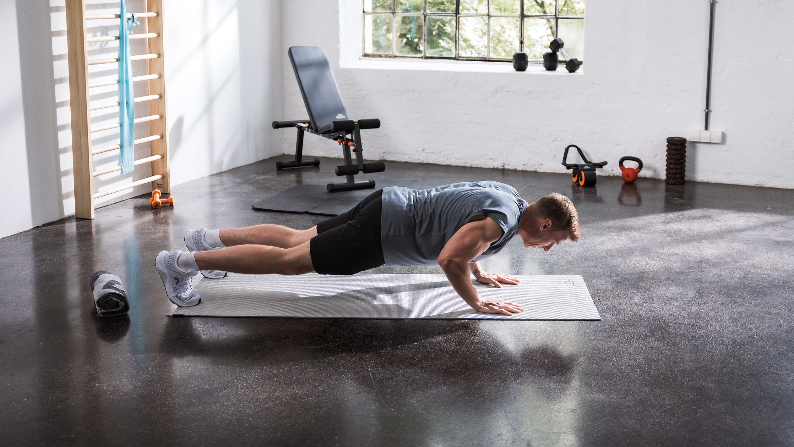 Mann macht Liegestütze auf einer Matte in einem Heim-Fitnessstudio mit verschiedenen Fitnessgeräten.