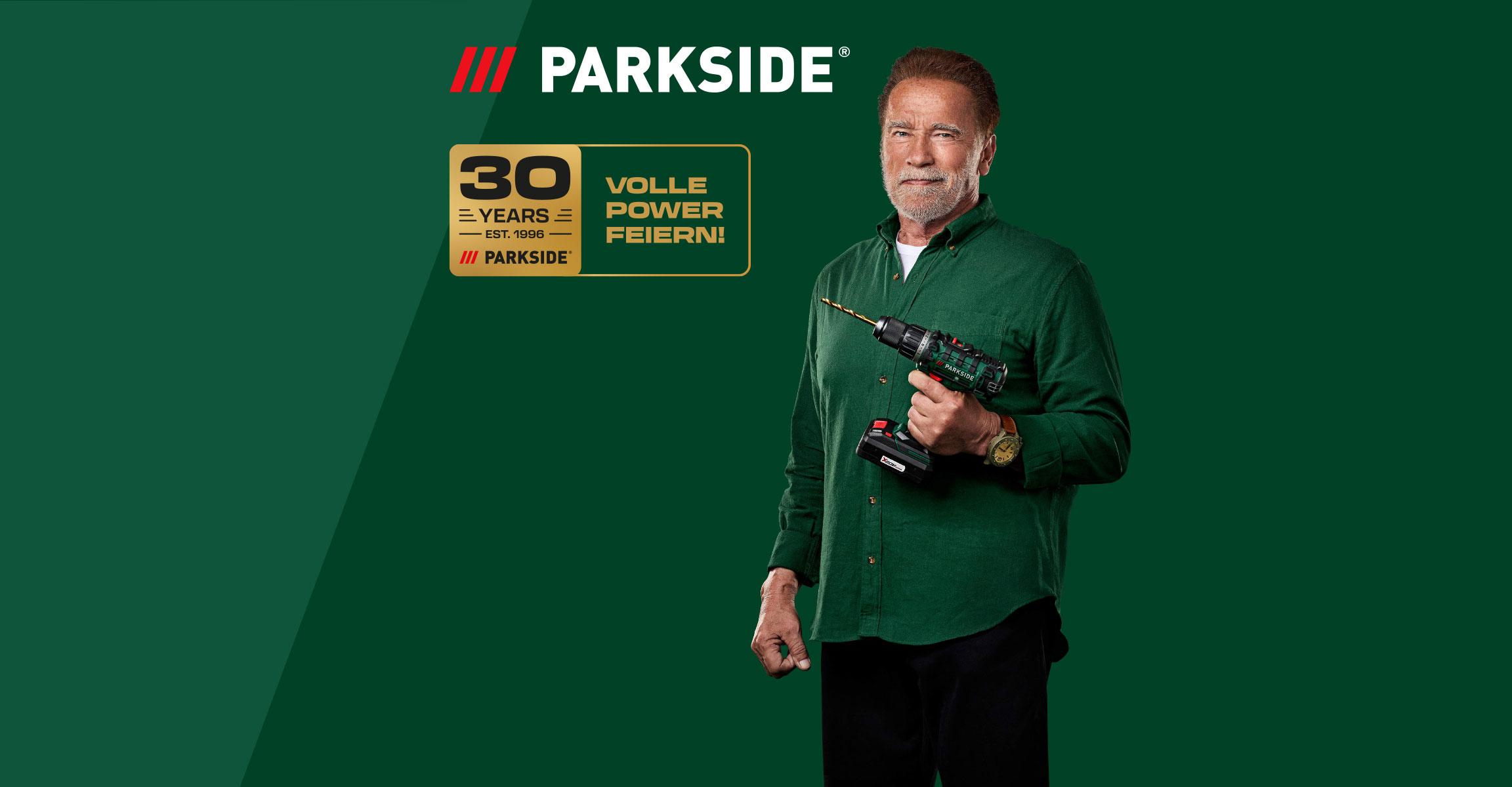 Arnold Schwarzenegger hält einen Akkuschrauber vor grünem Hintergrund mit einem 30-Jahre-Jubiläumslogo.