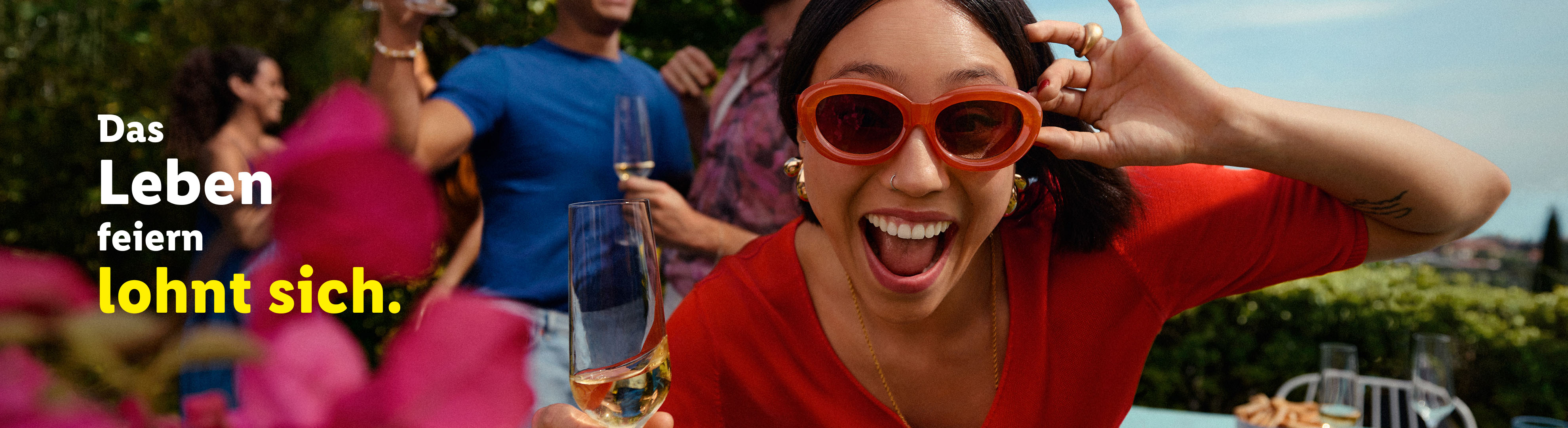 Eine Frau in roter Kleidung feiert mit Freunden und einem Glas Sekt.