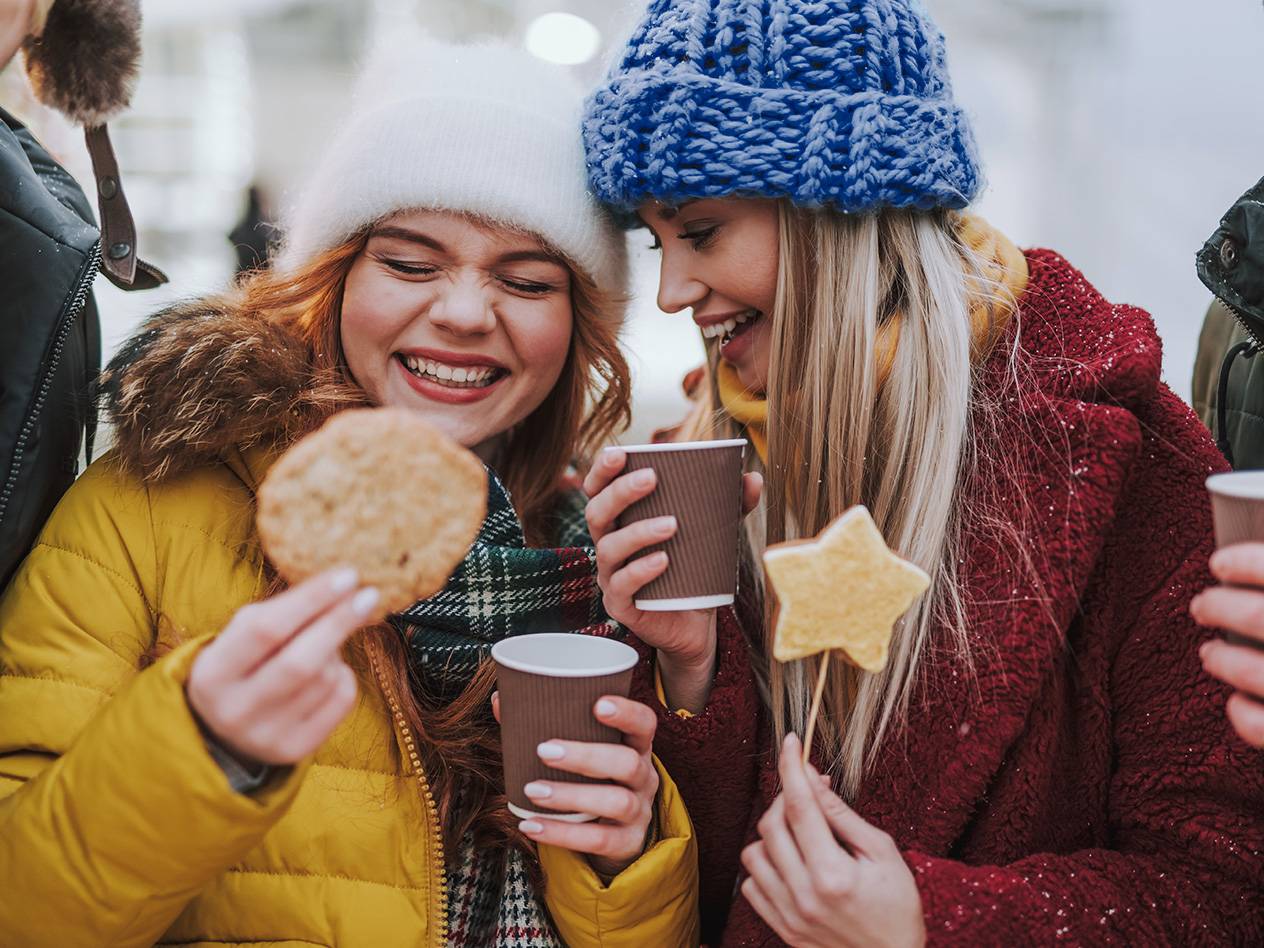 Zwei Mädchen auf der Straße halten einen Papierbecher und Kekse in der Hand.
