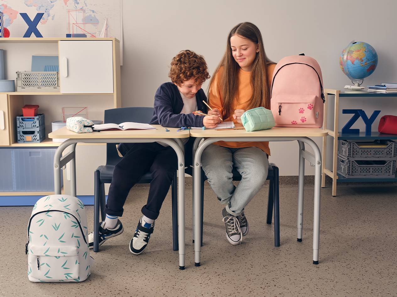 Zwei Kinder sitzen an einem Schreibtisch und lernen, mit Schulranzen und Federmäppchen.