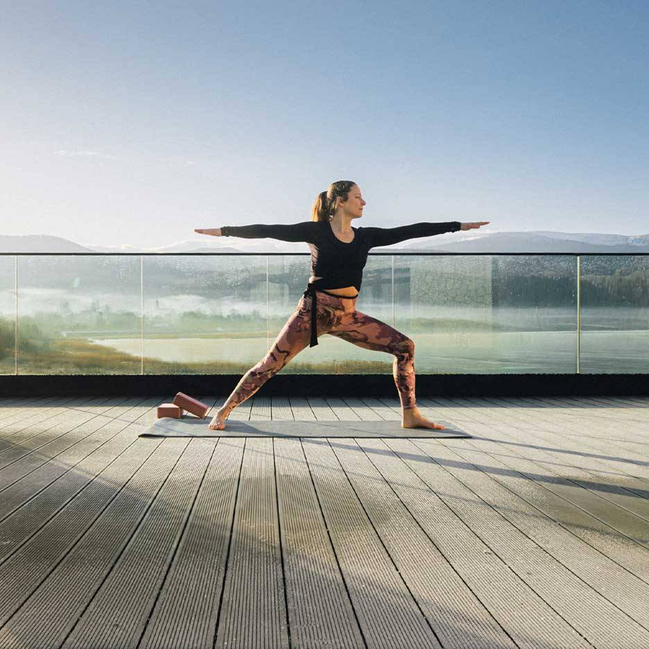 Frau in Sportleggings und Top macht Yoga auf einer Terrasse mit Aussicht.