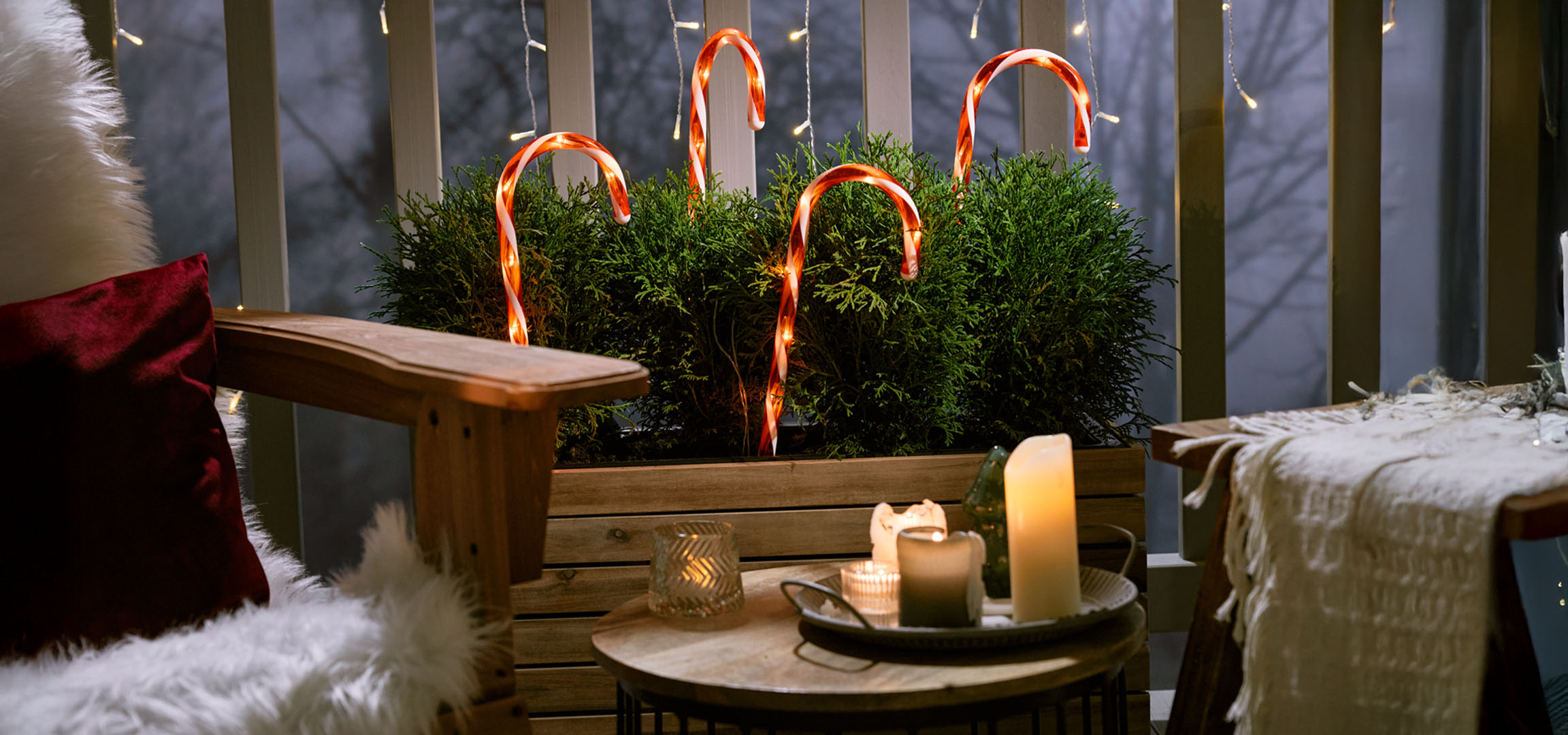 Weihnachtlich dekorierter Balkon mit Stuhl, Kerzen und Zuckerstangen.