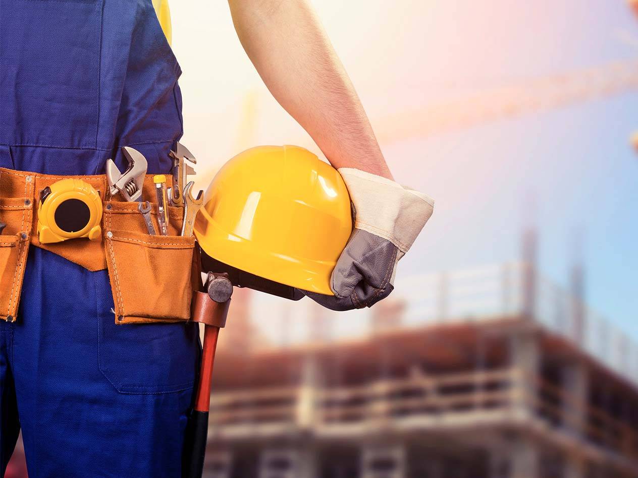 Bauarbeiter mit Werkzeuggürtel und gelbem Schutzhelm auf einer Baustelle.