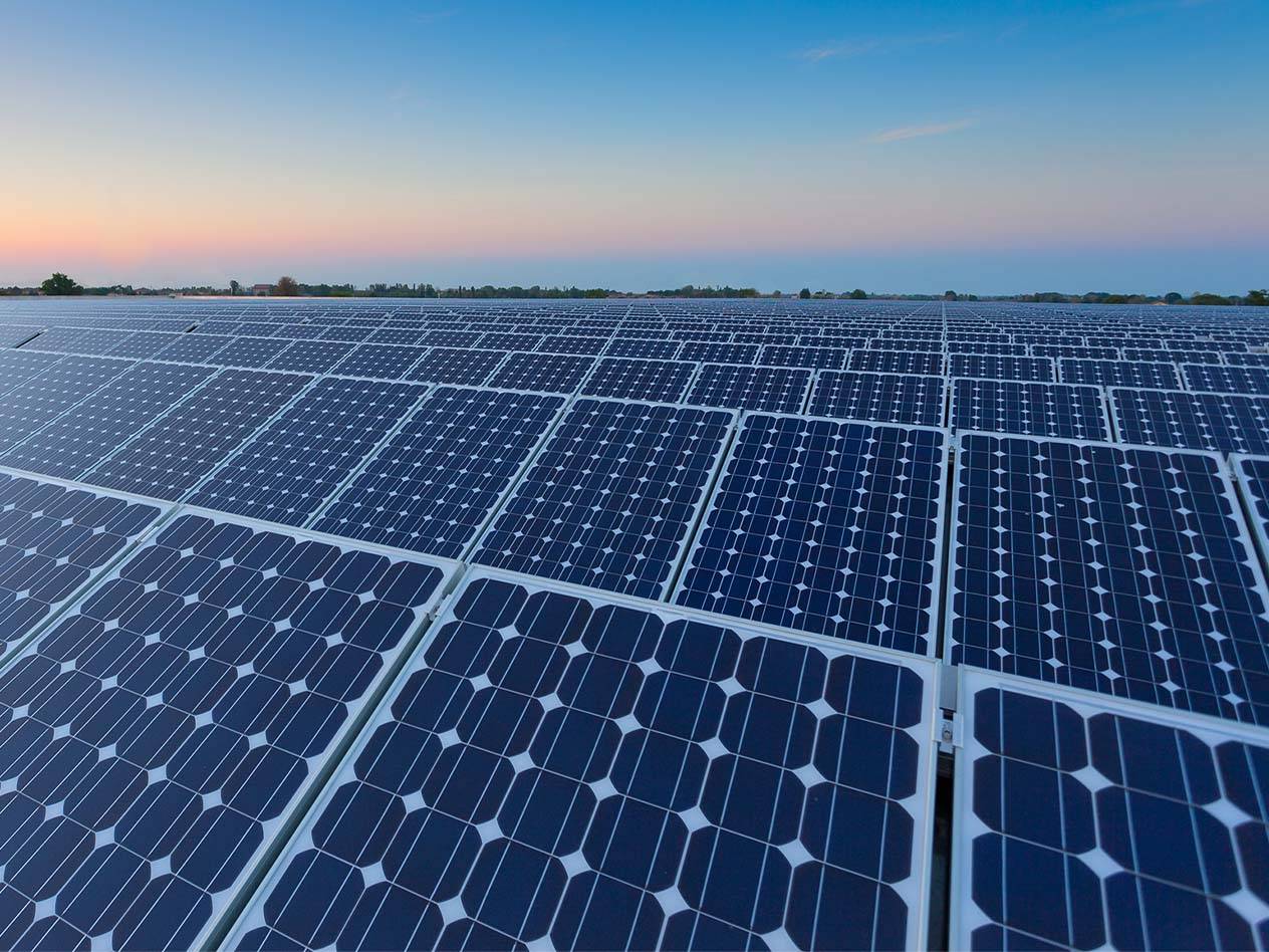 Weitläufiges Feld mit Solarmodulen unter einem blauen Himmel bei Sonnenuntergang.