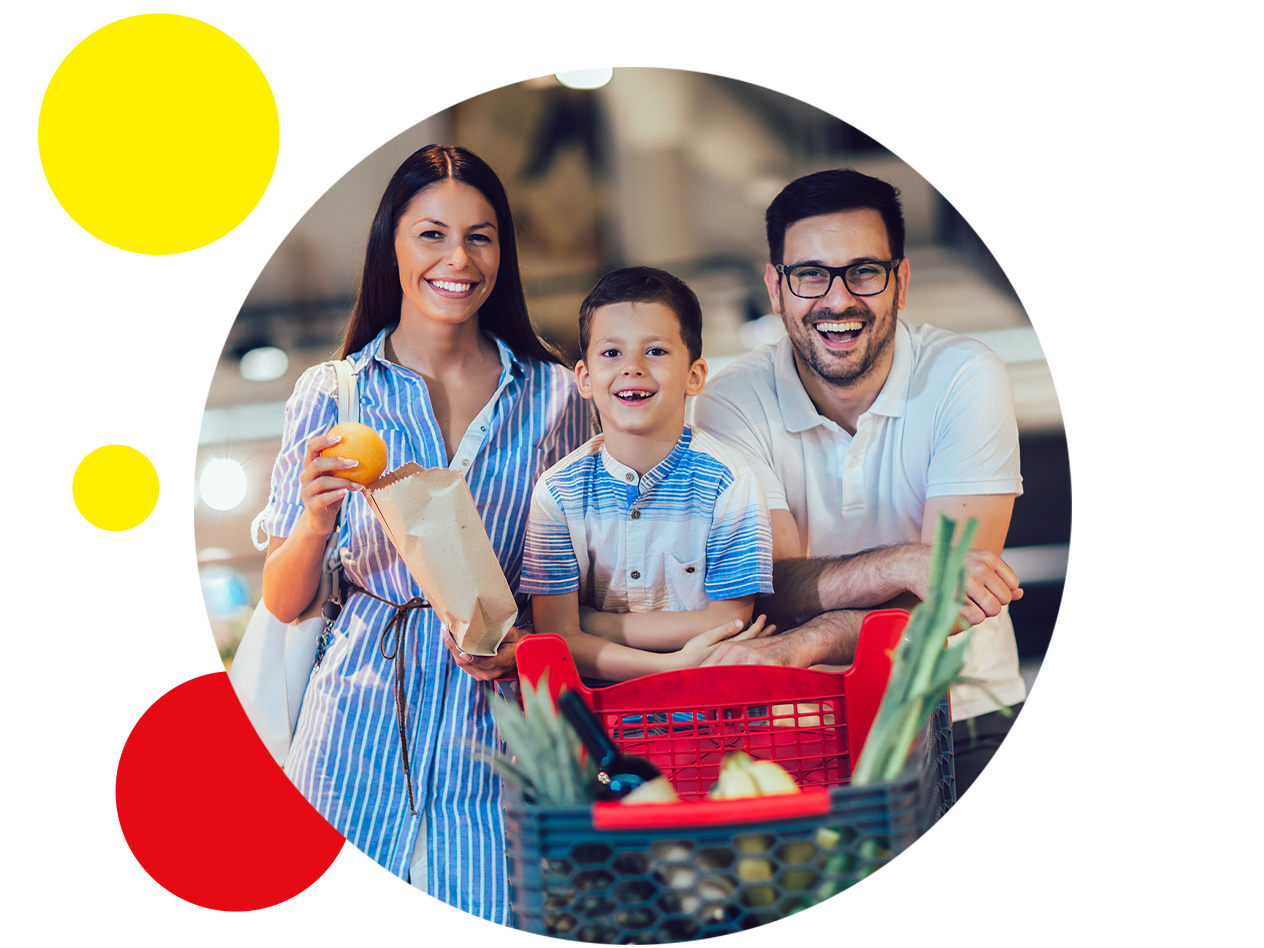 Eine lächelnde Familie mit einem Einkaufswagen voller Lebensmittel in einem Supermarkt.