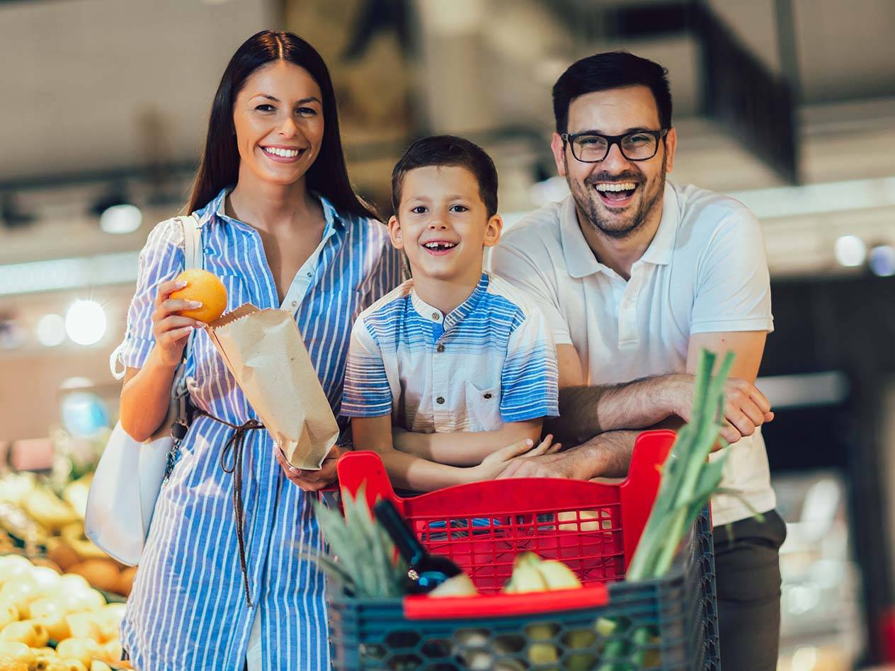 Eine lächelnde Familie mit einem Einkaufswagen voller Lebensmittel in einem Supermarkt.