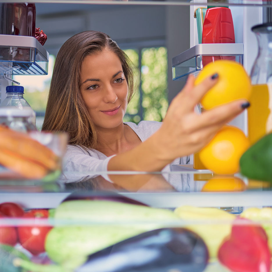 Eine Frau nimmt Orangen aus dem Kühlschrank.