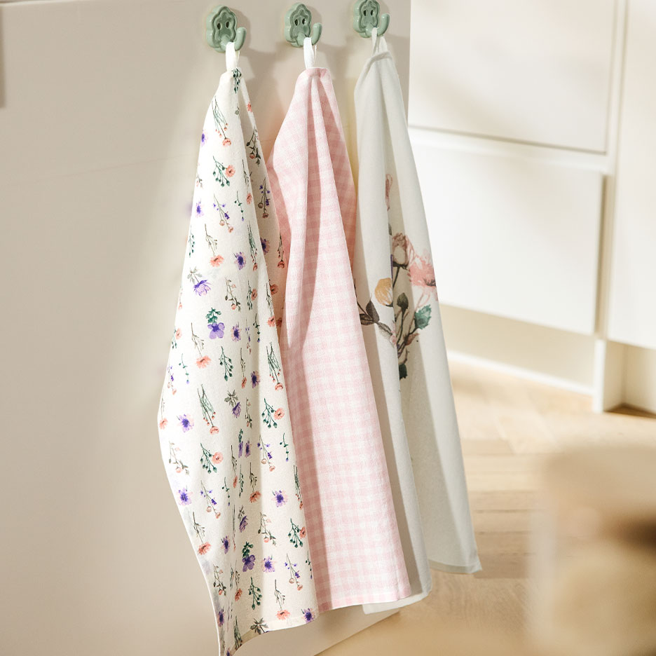 Drei gemusterte Geschirrtücher hängen an Haken vor einer hellen Wand.