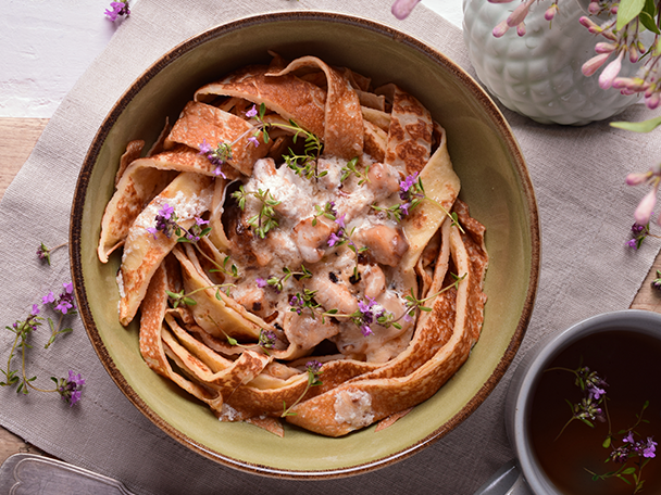 Pfannkuchenstreifen mit Pilzrahmsoße und Thymian in einer Schüssel, daneben eine Tasse Tee.