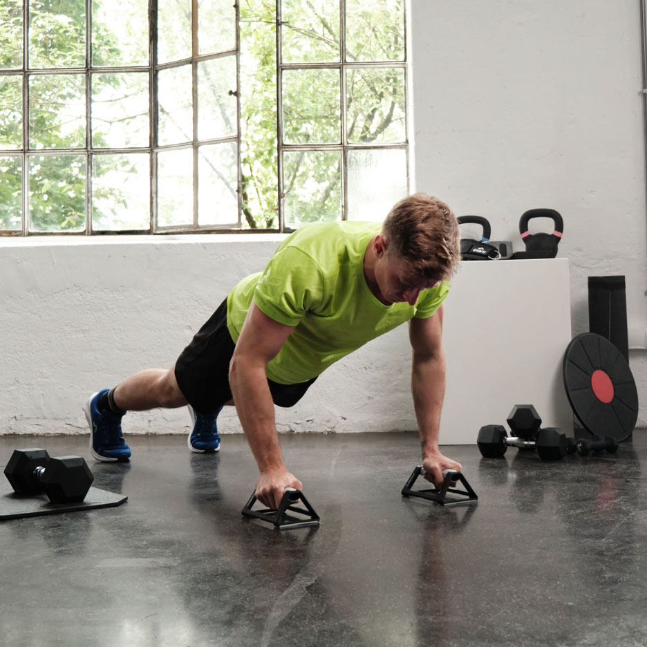Mann macht Liegestütze mit Griffen im Fitnessstudio.