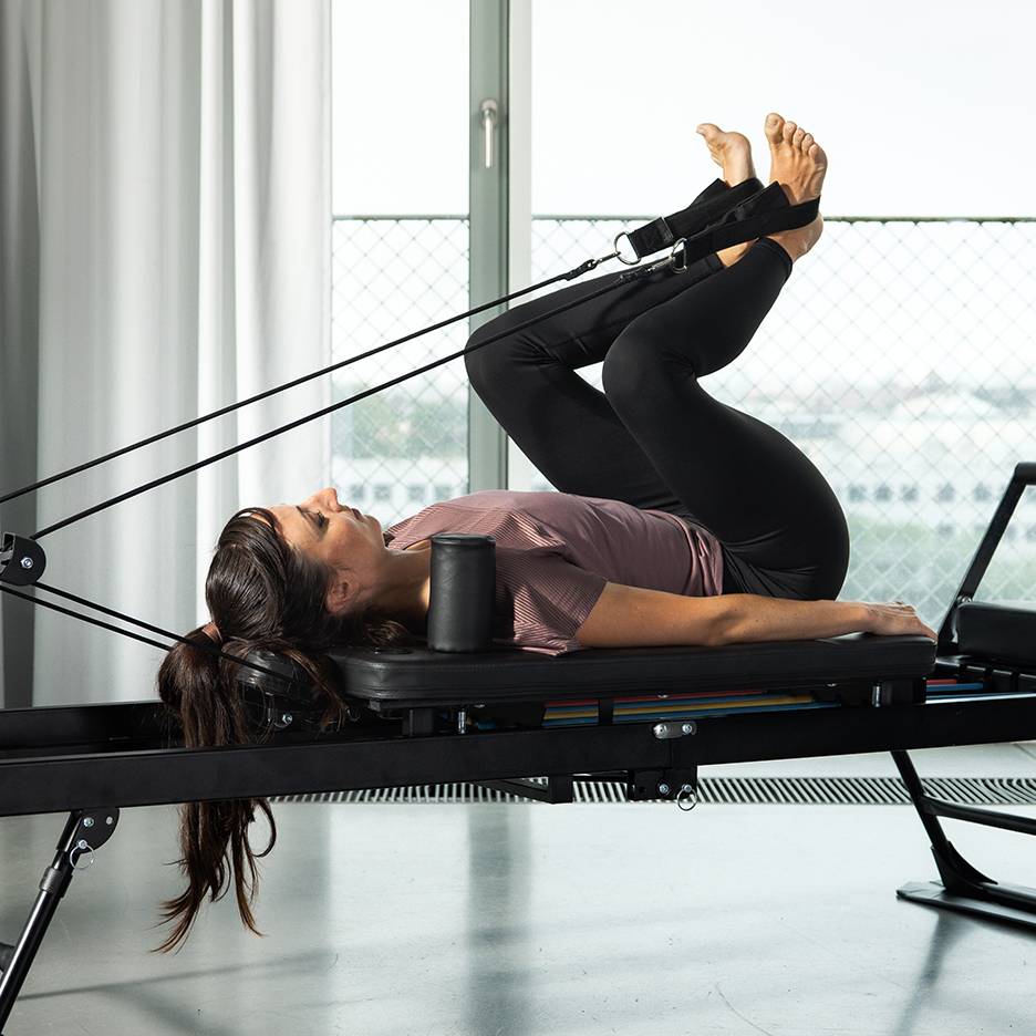 Frau trainiert Beine auf einem Pilates-Reformer mit Widerstandsbändern.