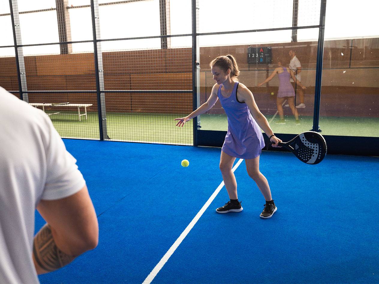 Frau im lila Sportkleid spielt Padel mit Schläger und Ball.