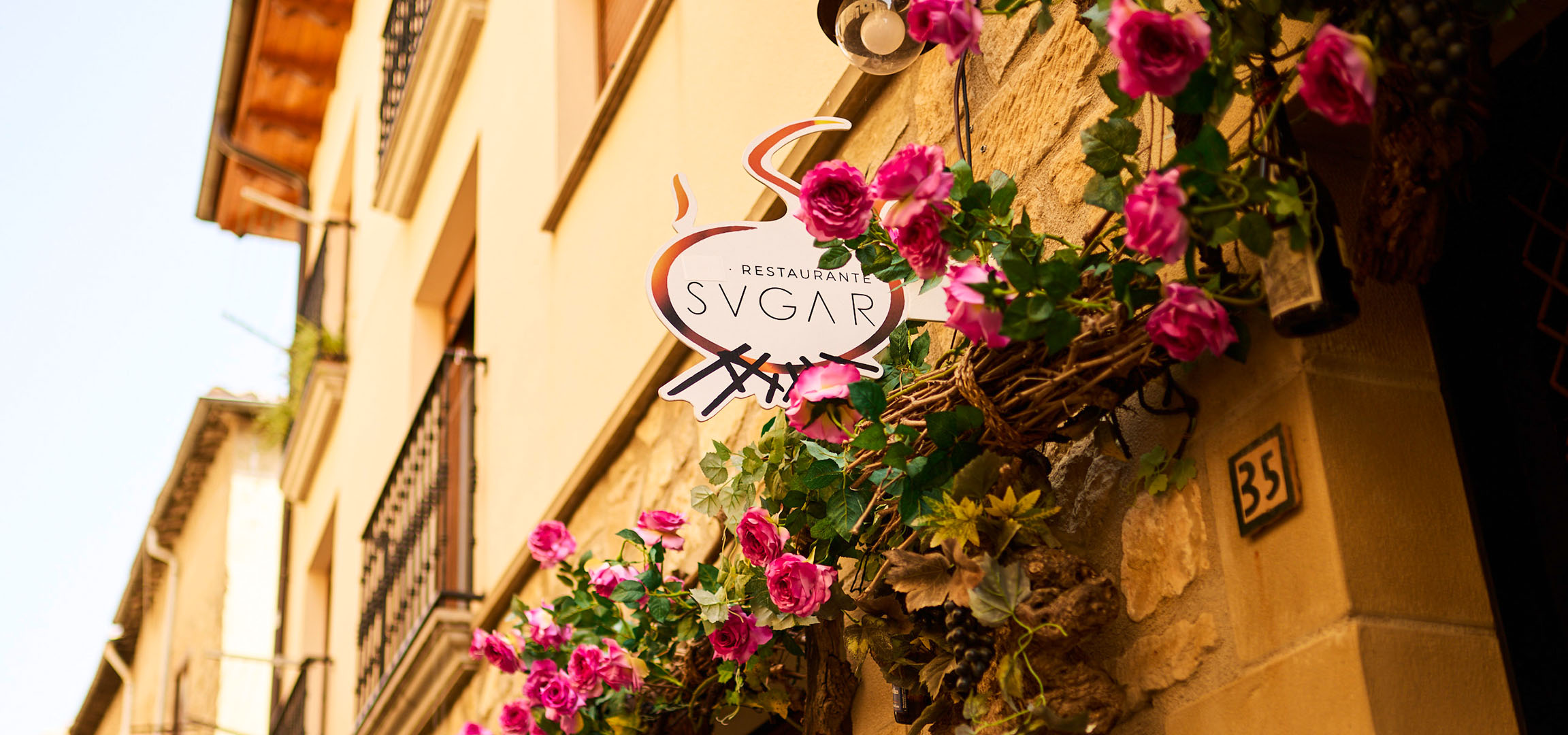 Restaurantschild „SVGAR“ mit rosa Blumen an einer Steinwand