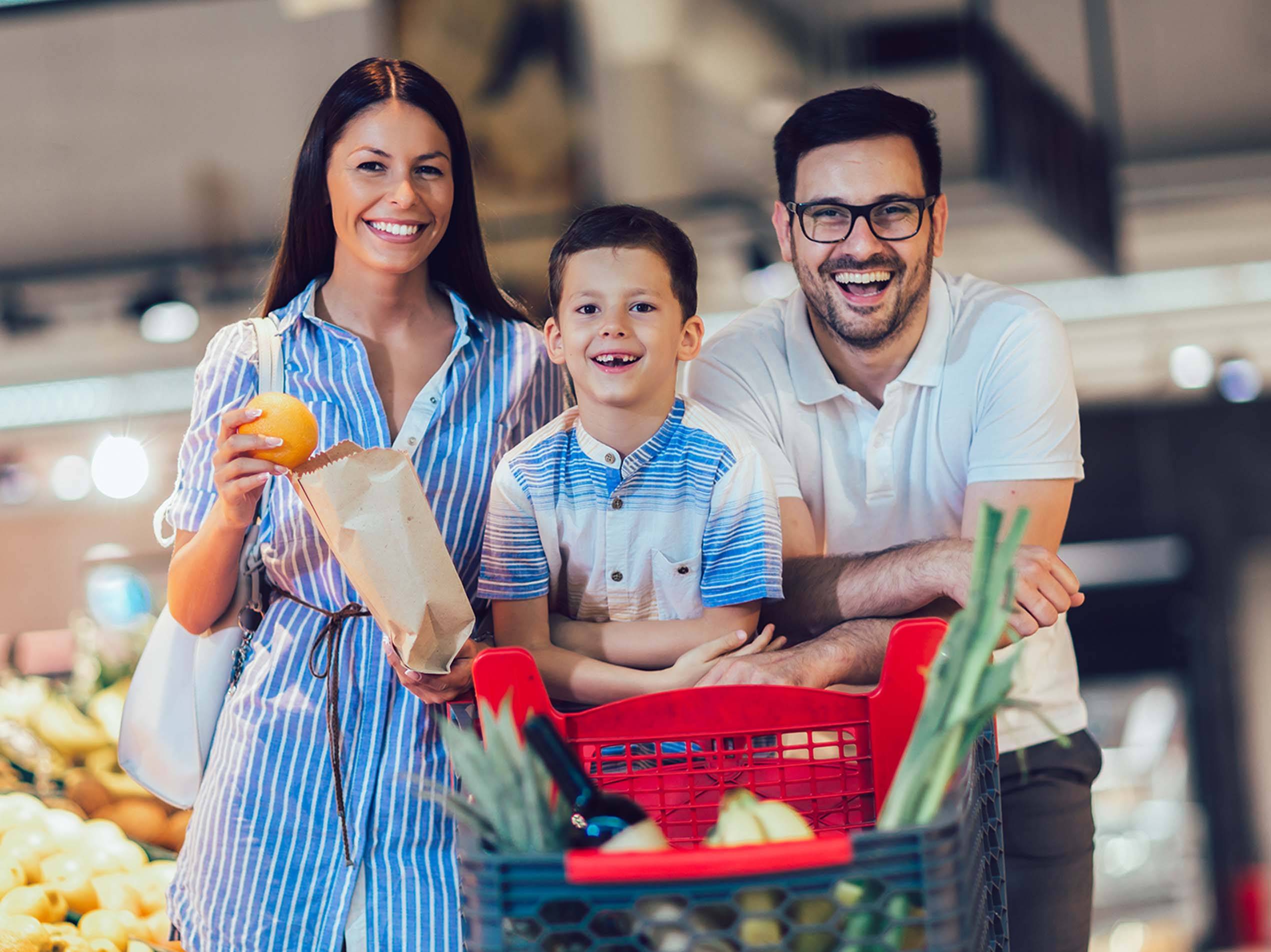 Eine lächelnde Familie mit einem Einkaufswagen voller Lebensmittel in einem Supermarkt.