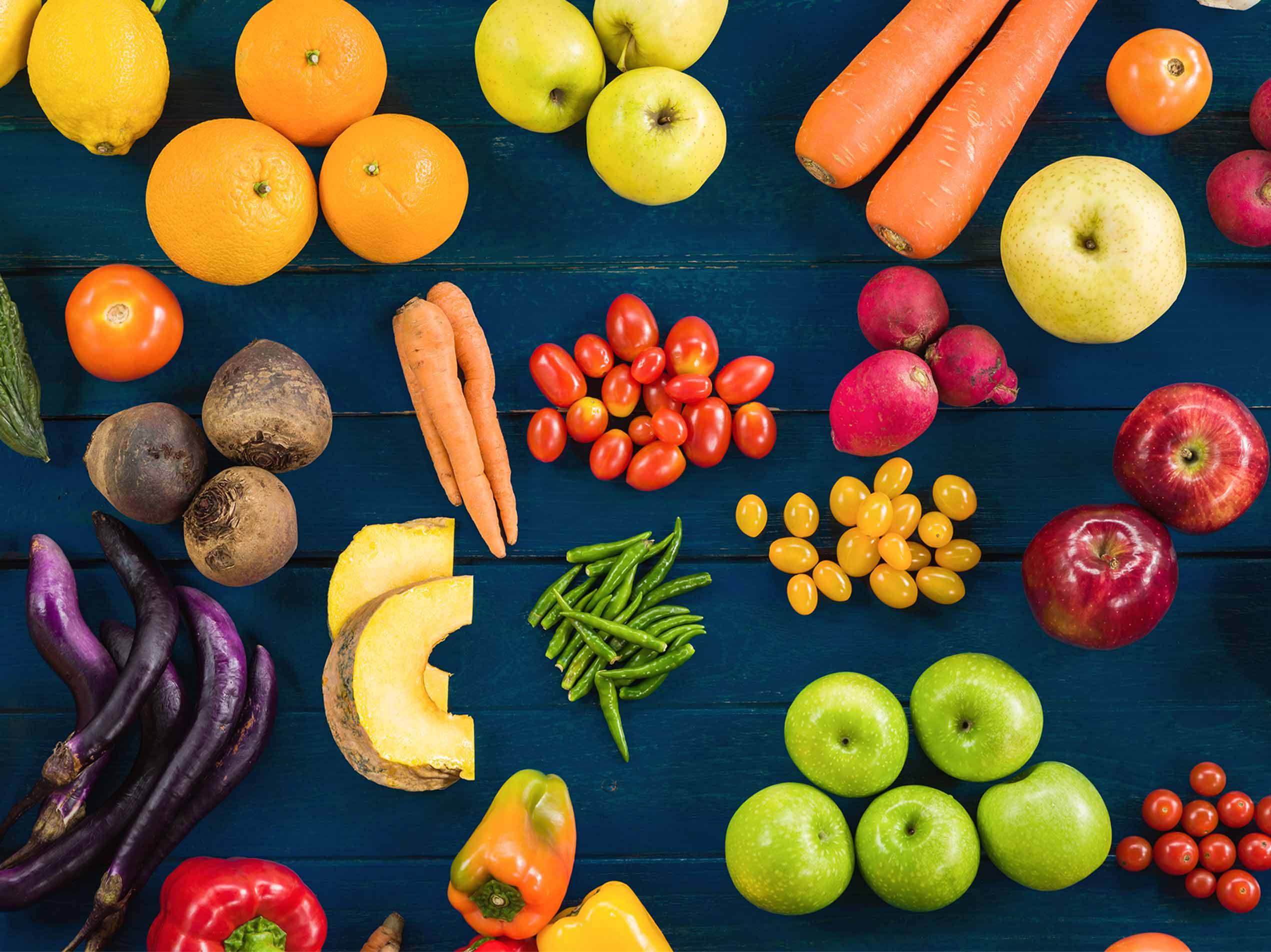 Eine bunte Auswahl an frischem Obst und Gemüse auf einem blauen Holztisch.