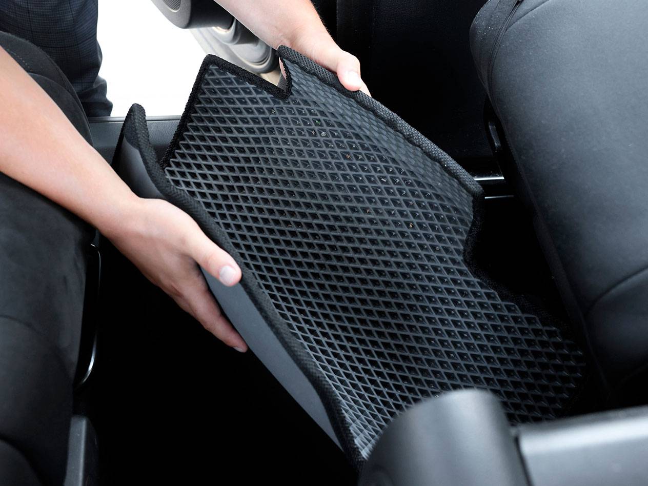 Person legt eine schwarze Gummi-Autofußmatte mit Rautenmuster in ein Fahrzeug.