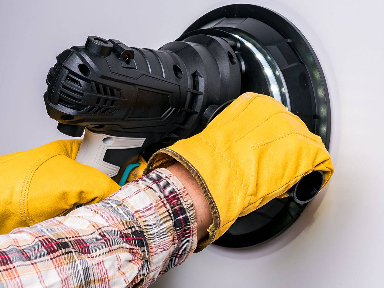 Elektrischer Wandschleifer mit LED-Licht, von einer Person mit Handschuhen benutzt.