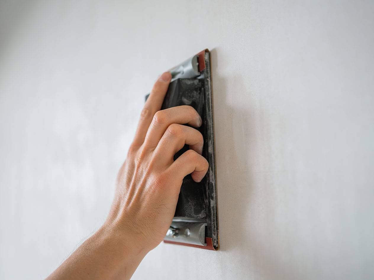 Hand schleift eine Wand mit einem Schleifklotz