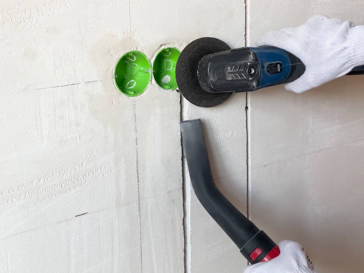 Elektrowerkzeug schneidet Nuten in eine Wand mit einem Staubsauger für Staub.