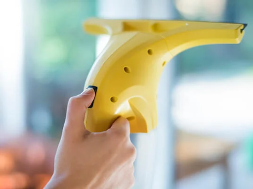 Hand hält einen gelben elektrischen Fensterreiniger, der ein Fenster putzt.