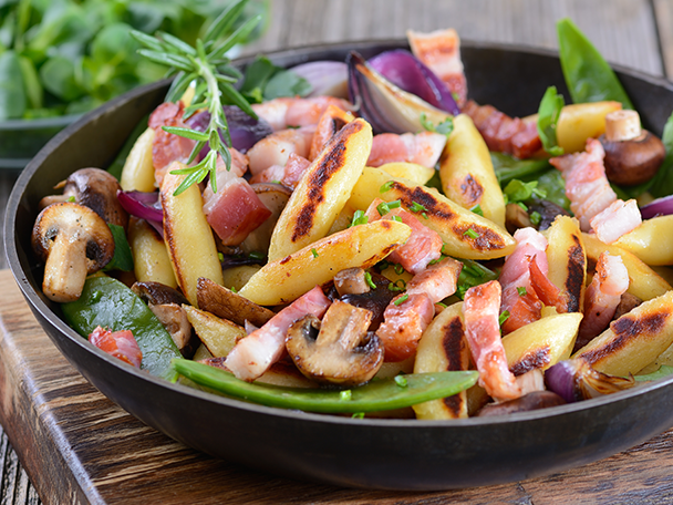 Bratkartoffeln mit Speck, Pilzen, Zwiebeln und Zuckerschoten in einer Pfanne