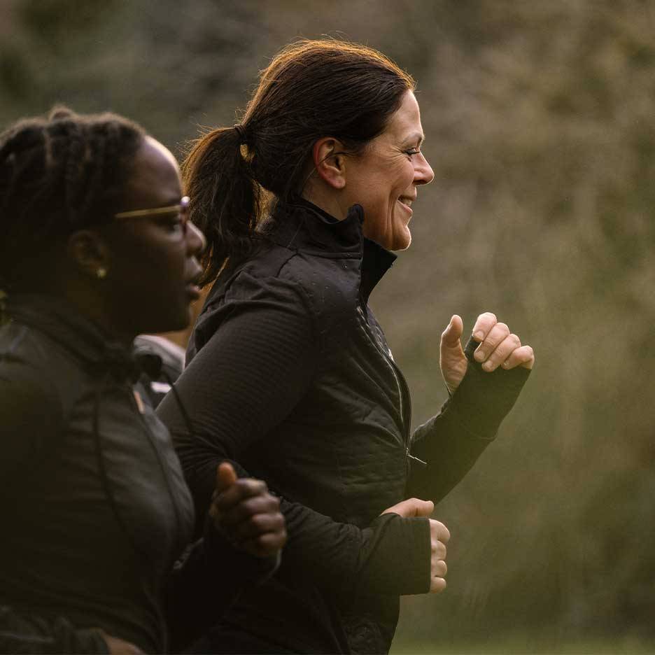 Zwei Frauen in Sportkleidung laufen draußen, eine lächelt.