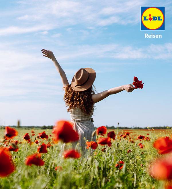 Eine Frau mit Hut genießt die Freiheit in einem Mohnblumenfeld - Lidl Reisen.