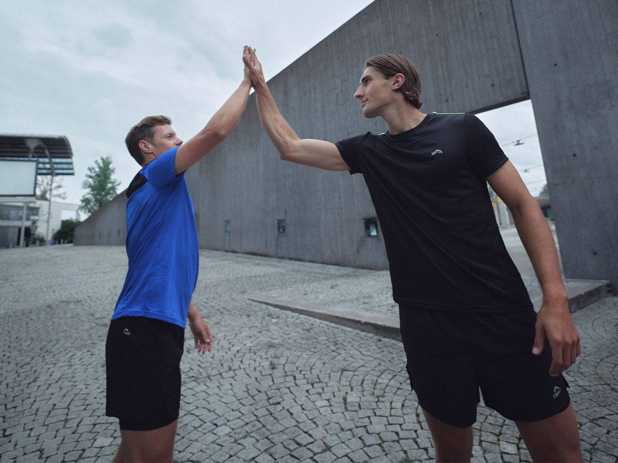 Zwei Männer in schwarzen und blauen Sport-T-Shirts und Shorts geben sich ein High-Five.