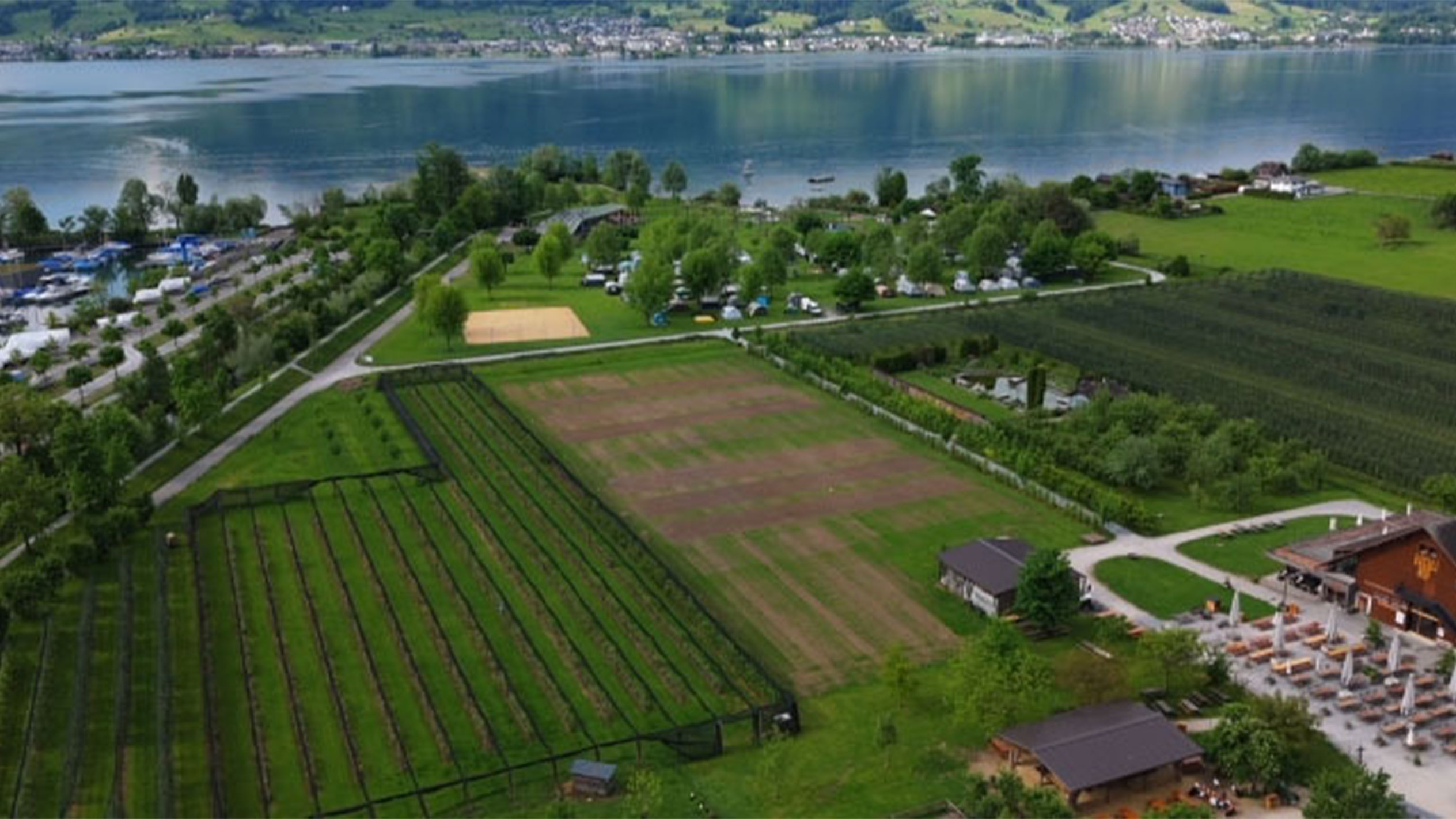 Luftbild eines Campingplatzes am See mit Gärten und Restaurant.