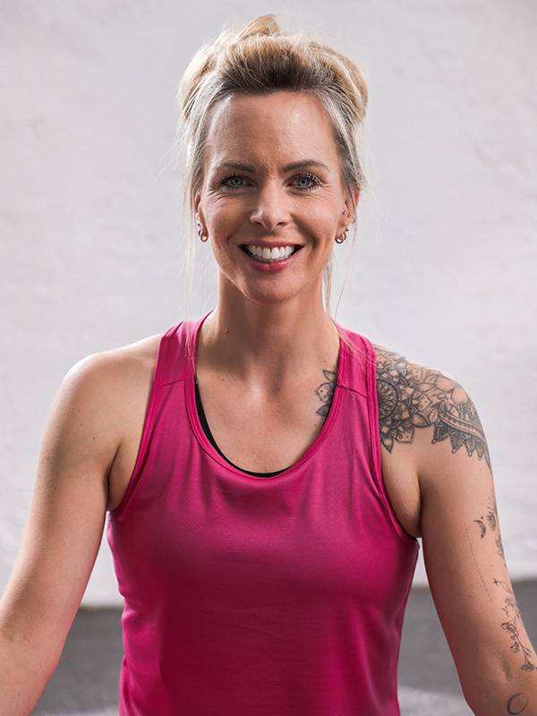 Eine lächelnde Frau in einem pinkfarbenen Sporttop mit Schultertattoos.
