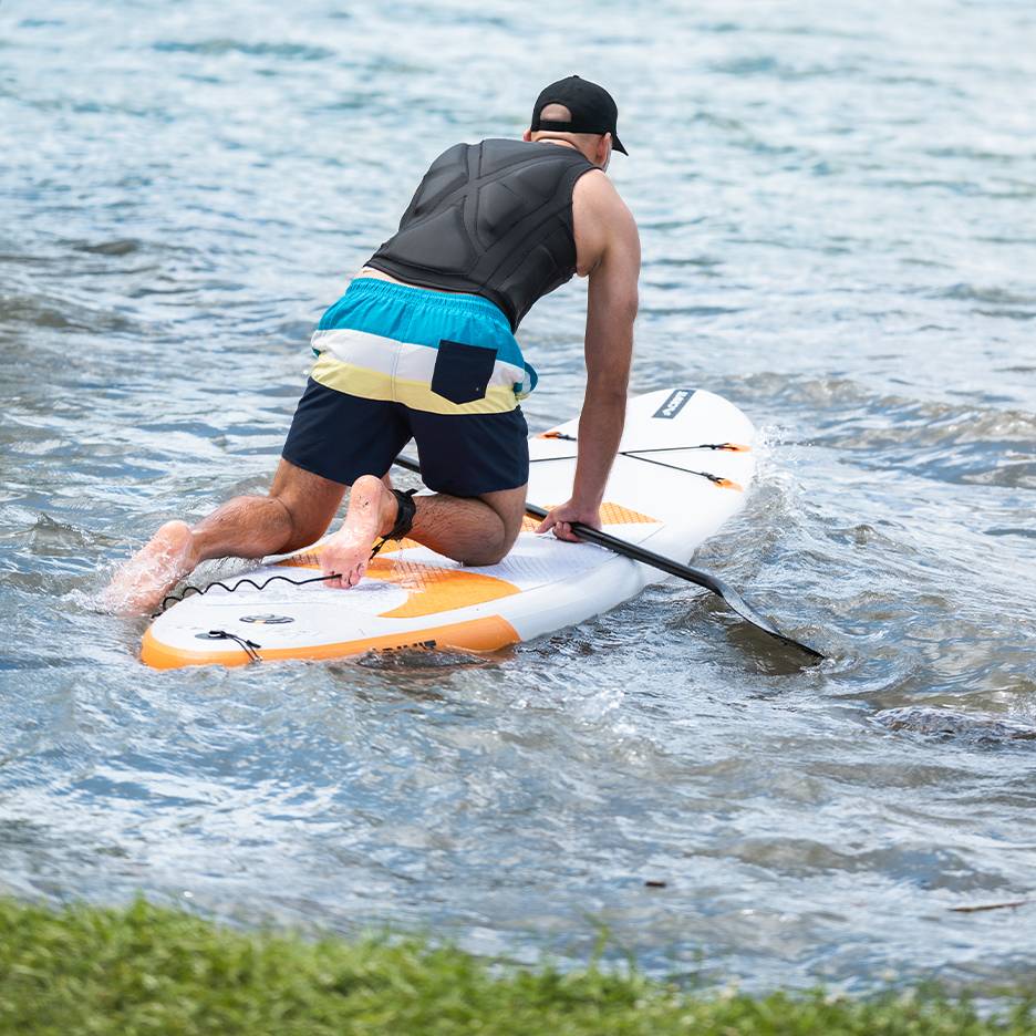Mann kniet auf einem Paddleboard mit Paddel im Wasser.