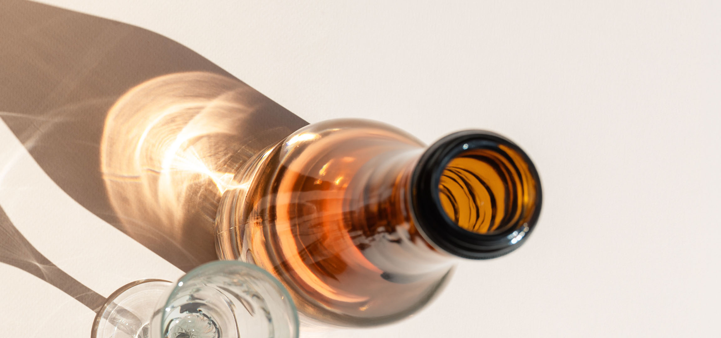 Gläser und Flasche mit Schatten und Lichtreflexionen auf hellem Hintergrund