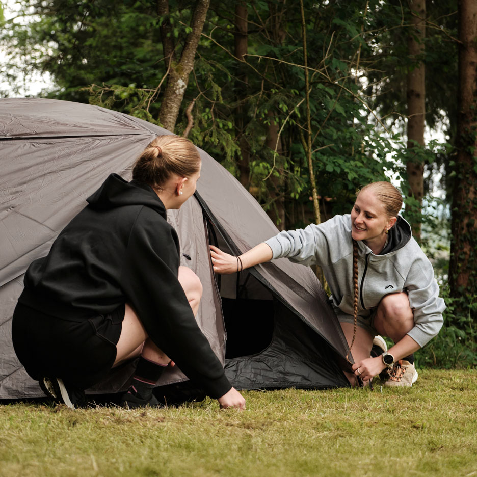 Zwei Frauen bauen ein Zelt im Wald auf.