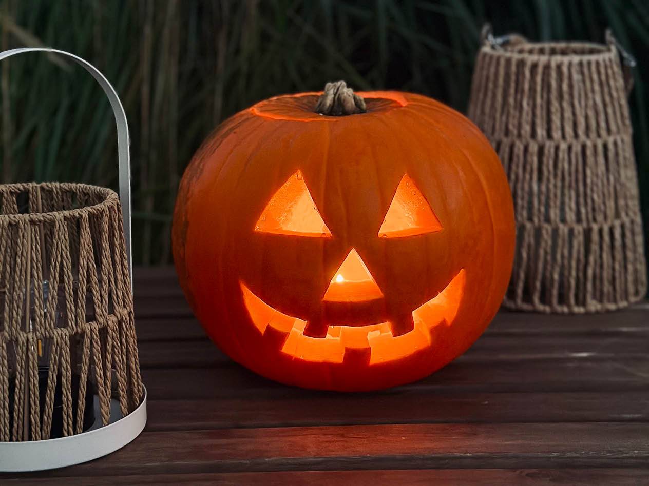 Leuchtender Halloween-Kürbis mit geschnitztem Gesicht auf einem Holztisch, umgeben von Laternen.