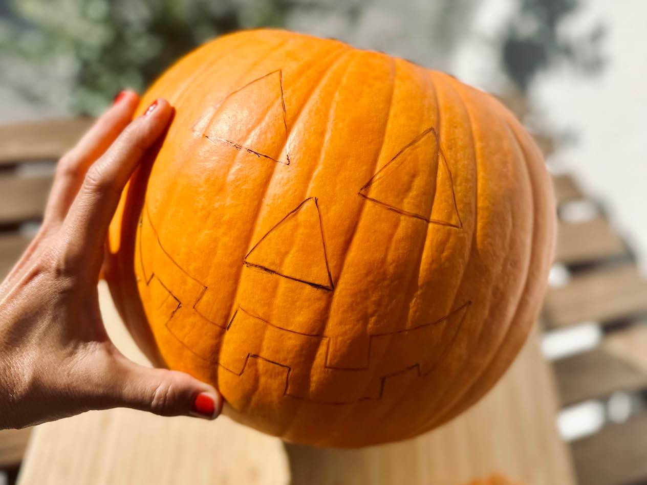 Eine Hand hält einen Kürbis mit einem aufgemalten Jack-o'-Lantern-Gesicht.