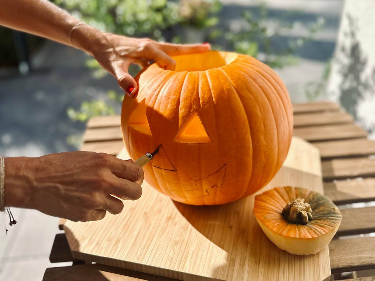 Eine Person schnitzt einen Kürbis auf einem Holzbrett, um eine Halloween-Laterne zu machen.