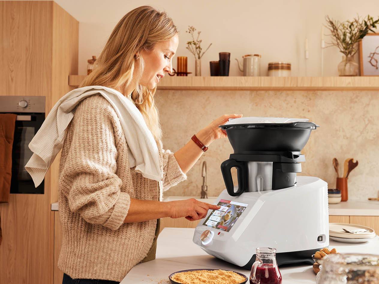 Eine Frau bedient eine weiße Küchenmaschine mit Touchscreen in einer modernen Küche.