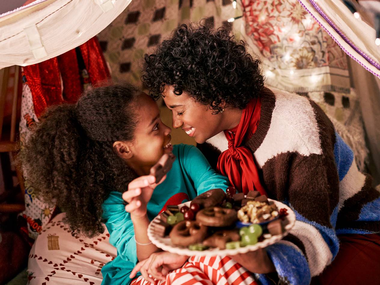 Mutter und Kind teilen sich Süßigkeiten und Obst in einem gemütlichen Zelt.