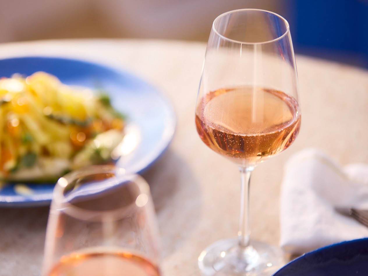 Ein Glas Rosé-Schaumwein steht auf einem Tisch neben einem Teller mit Salat.