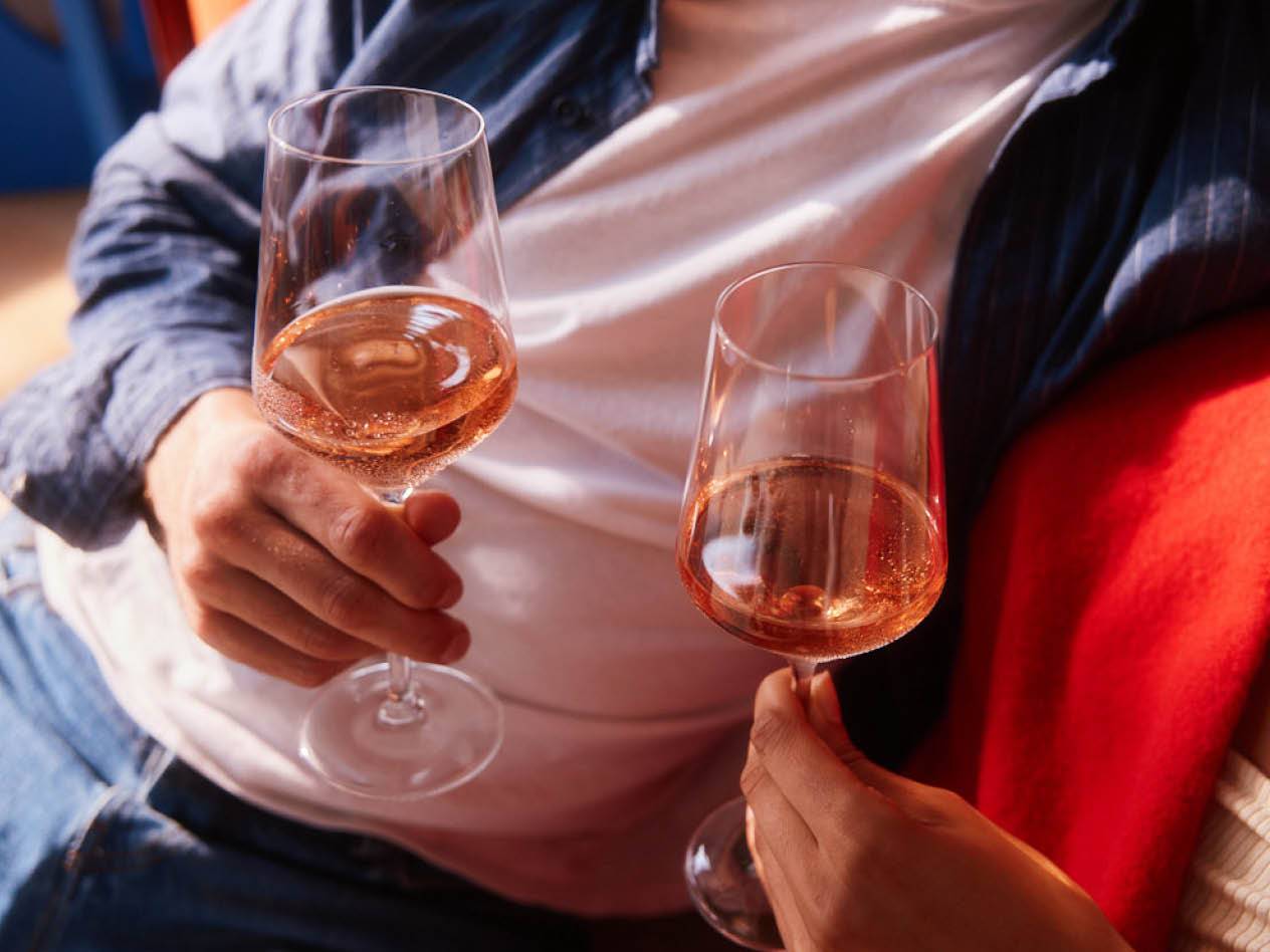 Zwei Gläser Roséwein werden von einem Paar auf einem Sofa genossen.